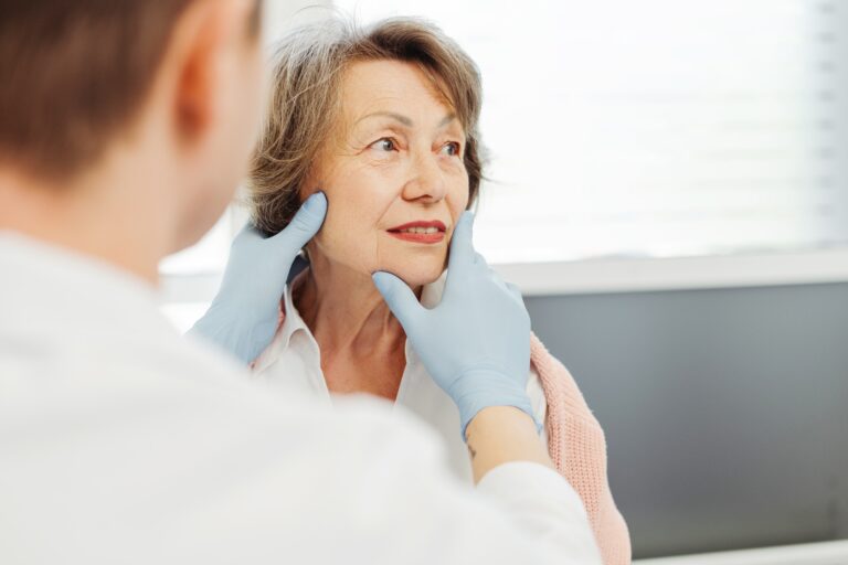 Attractive senior woman, patient talking to cosmetologist doctor, he touches her face, lifting